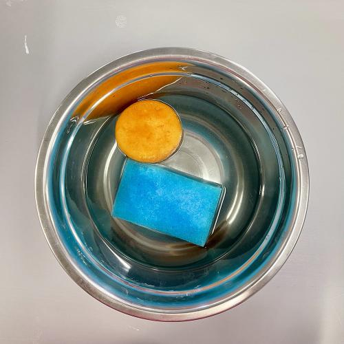 round orange and square blue sponges in bowl of water